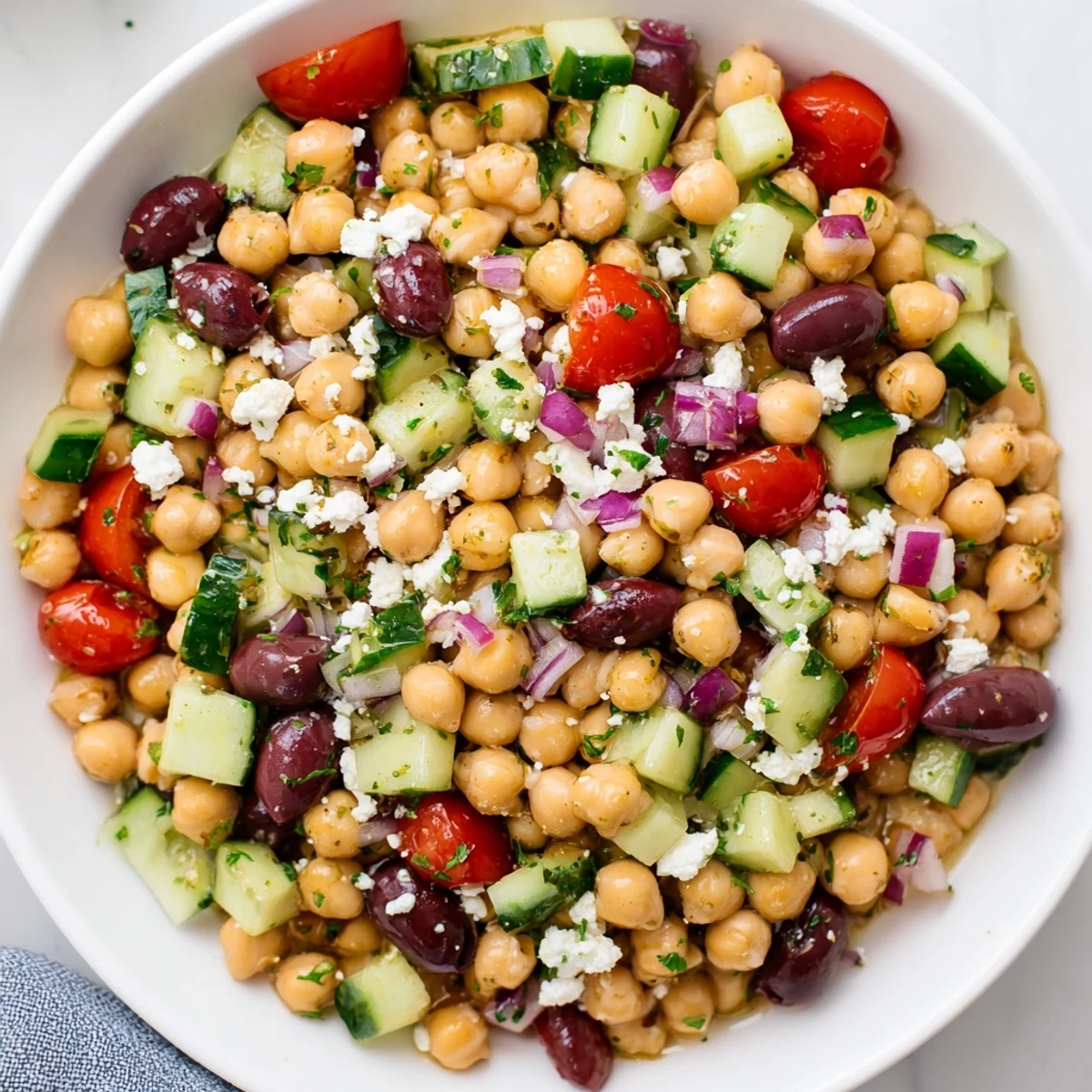 This fresh Mediterranean Chickpea Salad is piled high, displaying tomatoes, cucumbers, and Kalamata olives.