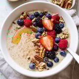 Steaming Millet Porridge With Berries served in a rustic ceramic bowl, featuring a creamy texture and a drizzle of golden honey.