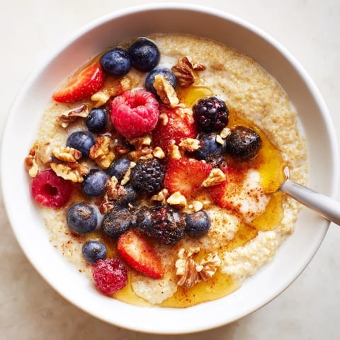 A warm bowl of Millet Porridge With Berries, topped with blueberries, raspberries, and a sprinkle of chopped walnuts for a nutty crunch.