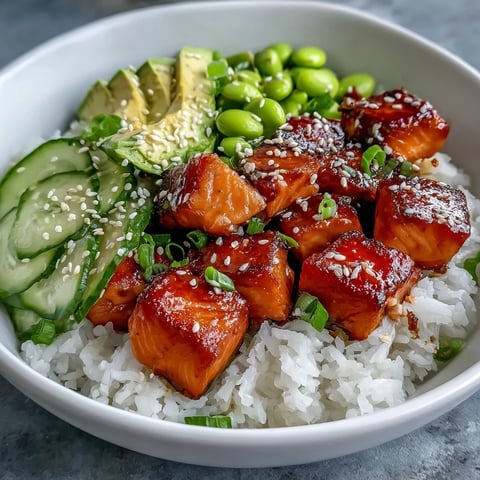 Flaked baked salmon sits atop fluffy jasmine rice in a colorful Salmon Rice Bowl garnished with edamame, cucumber, and avocado slices.  
