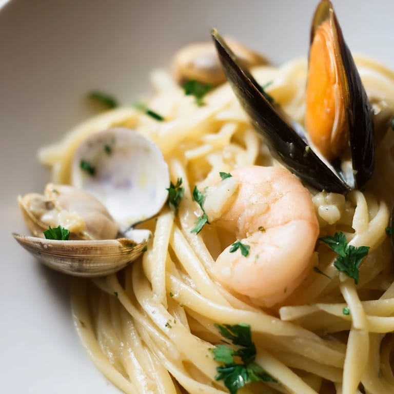 A plated portion of Seafood Linguine featuring plump mussels, shrimp, and clams, glistening with buttery sauce and a sprinkle of red pepper flakes.